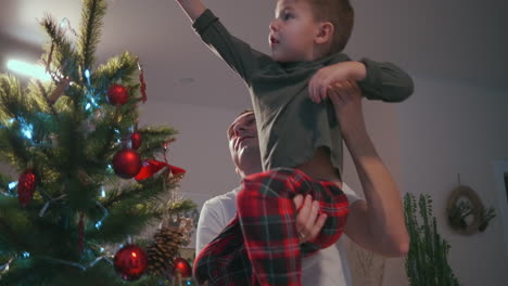 Father-lifts-boy-to-dress-Christmas-star-on-top-of-Christmas-tree.-High-quality-4k-footage